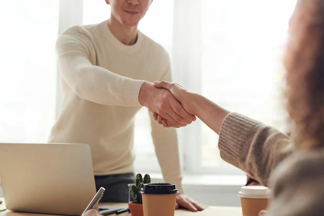 Two people shaking hands over a table.