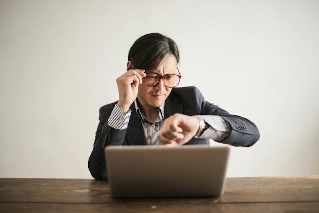 A person at a laptop checking their watch.